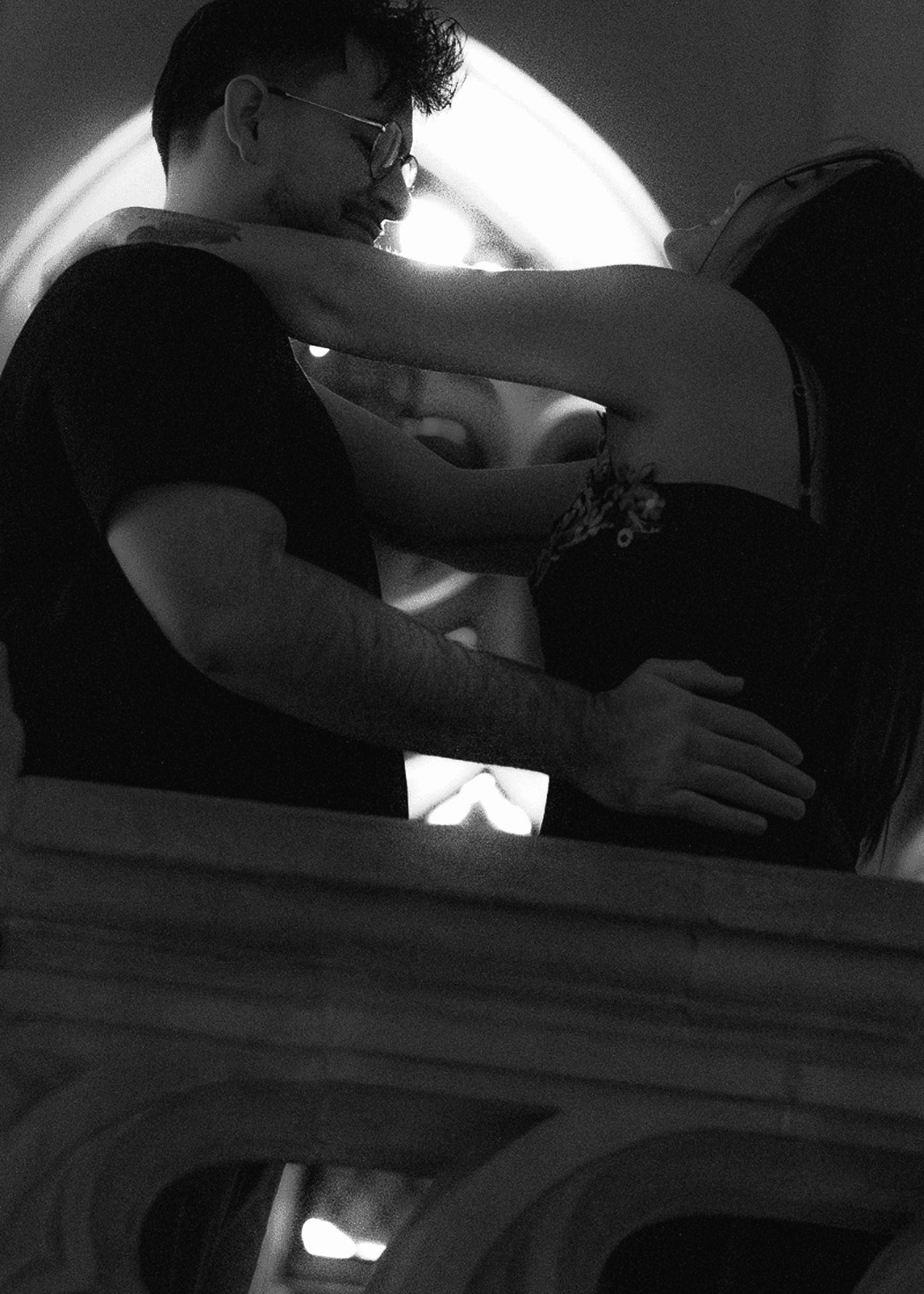 Ethan and Amanda embracing beneath an arched church window, lit from behind.
